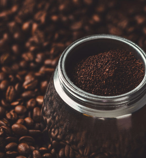 Ground coffee in a moka pot surrounded by coffee beans