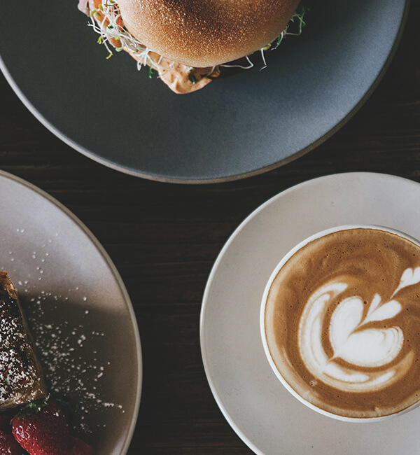 A sandwich, cake and latte served on plates