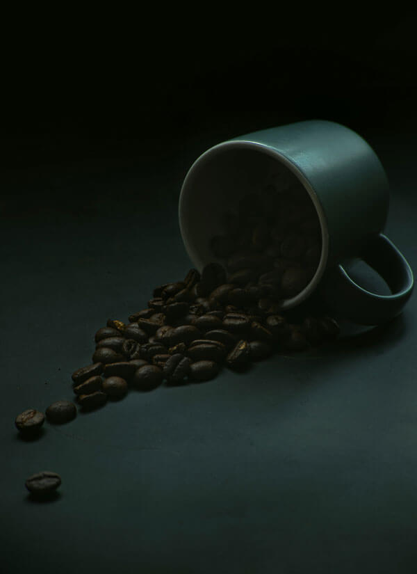 Coffee beans spilling from a ceramic mug